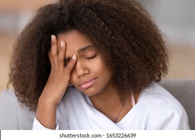 Sad or bored african american teen girl feeling headache or sleepiness touching head, upset depressed black teenager crying alone at home, ill sick mixed race school kid suffer from bullying abuse