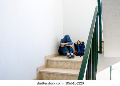 Sad boy with backpack sitting alone in the corner in the staircase - Powered by Shutterstock