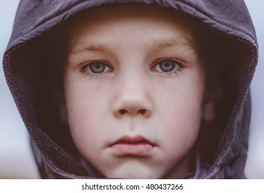 Sad Boy In A Black Hood. Closeup. Kid With Big Blue Eyes And Long Lashes Sadly Looking At The Camera Outdoors