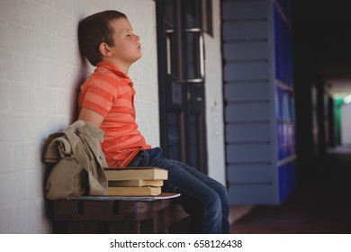 Sad boy with eyes closed sitting on bench by wall in corridor at school - Powered by Shutterstock