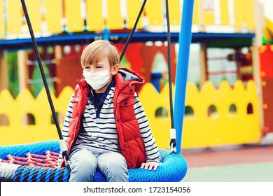 Sad Boy In Face Mask Playing Outdoors. Bored Child At Empty Playground Outside. Coronavirus Quarantine. Child Wearing Safety Mask. Coronavirus Prevention. Sad Kid Riding On A Swing. Real Life 2020.