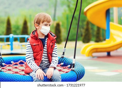 Sad Boy In Face Mask Sitting On Swing Alone. Bored Child At Empty Playground. Quarantine. Child Wearing Safety Mask. Coronavirus Prevention. Child Riding On A Swing. Real Life 2020.  