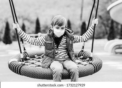 Sad Boy In Face Mask Sitting On Swing Alone. Coronavirus Prevention.Sad Kid Riding On A Swing. Real Life 2020. Sad Lonely Boy. Bored Child At Empty Playground. Quarantine.Child Wearing Safety Mask Ou