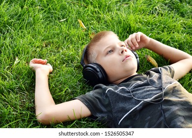 Sad Boy In Headphones Outdoor Summer. Melancholy Musical Mood. The Child Alone Secluded Himself On The Grass. Problems Of Teenage Boys. Relax And Listen To Music On Headphones.