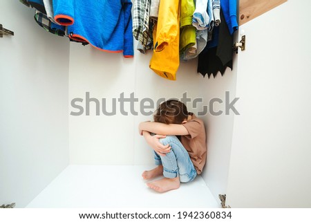 Sad boy hiding in the wardrobe. Domestic violence and abused concept. Unhappy childhood. Upset kid crying in his room.