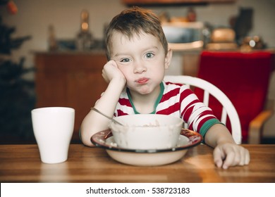 Sad Boy And A Plate Of Porridge. Upset Child At The Table. The Concept Of Eating Disorders. Healthy Porridge On Christmas Morning Instead Of A Festive Breakfast