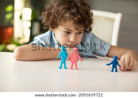 A sad boy plays with plasticine figurines of a family where parents and child are separate, the concept of abandoned children, adoption. High quality photo