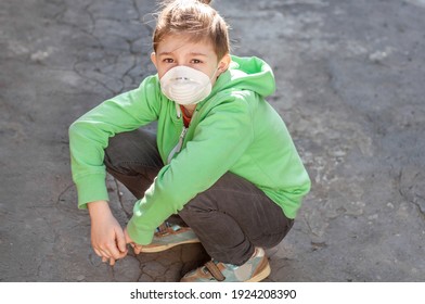 Sad Boy In A Respiratory Protective Mask Is Squatting On The Pavement. Coronavirus Covid19. Quarantine And Isolation. Schoolboy Teen Misses In Quarantine. Cancellation Of Entertainment. Spring Fashion