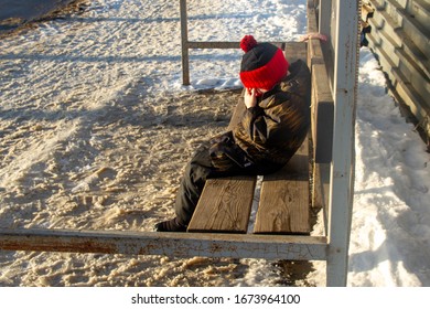 A Sad Boy Sits On A Bench At A Bus Stop And Cries. The Boy Lost His Family And Was Left Alone.