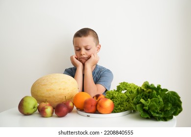 A Sad Boy Sits At The Table Next To Fresh Vegetables And Fruits