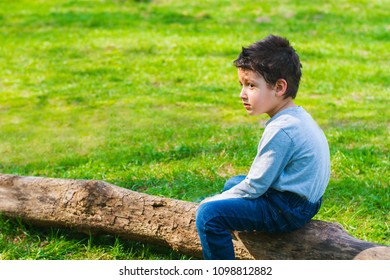 sad boy sitting alone on a log in the meadow