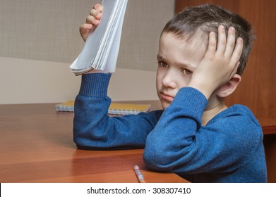 Sad Boy Sitting At School Desk With Notebook In Hand