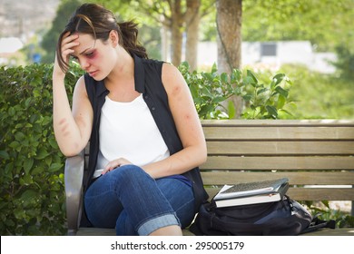 Sad Bruised and Battered Young Woman Sitting on Bench Outside at a Park.