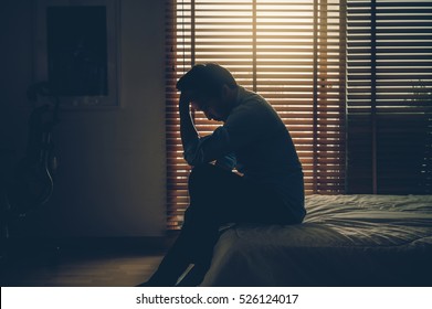Sad businessman sitting head in hands on the bed in the dark bedroom with low light environment, dramatic concept, vintage color tone