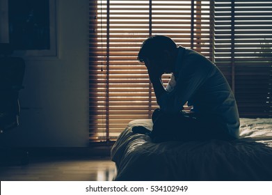 Sad businessman sitting head in hands on the bed in the dark bedroom with low light environment, dramatic concept, vintage tone color