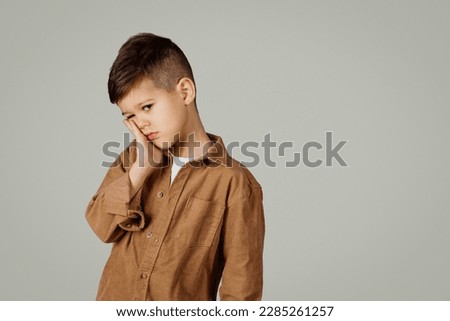 Sad caucasian 6 years old little boy presses hand to cheek, suffers from pain in tooth isolated on gray studio background. Teeth decay, dental problems, child emotions and facial expression