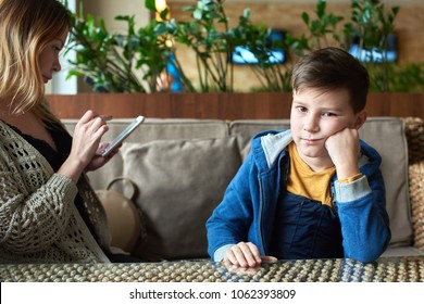 Sad Caucasian boy is feeling lonely because of his mom is ignoring him spending time using cellphone. 