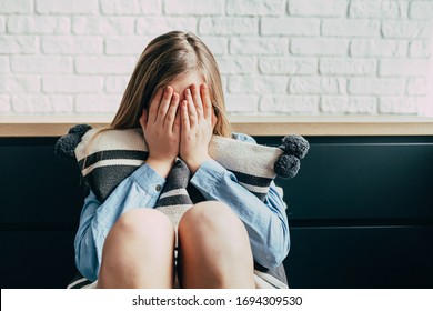 Sad Caucasian girl in depression hugs a pillow and closes her eyes with her hands on a background of a white brick wall. Thinks about the problems and puberty of a teenage girl. Adolescence period - Shutterstock ID 1694309530