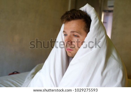 Sad caucasian man sitting on his bed with his head covered with blanket. Depression and troubles about life problems