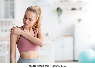 Sad Caucasian Young Blonde Lady Suffering From Injury And Pain In Shoulder After Workout At Home, Empty Space. Sports And Health Problems, Self Exercise Indoor During Covid-19 And Facial Expression