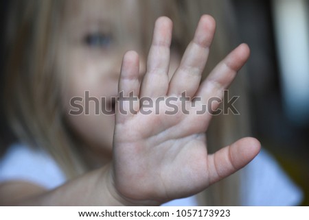 Sad child girl covers her face with her hand from violence