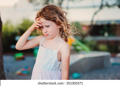 Sad Child Girl With Headache On Summer Playground, Touching Head