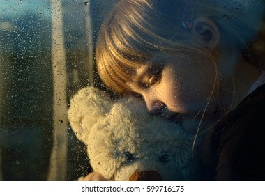 Sad Child Hugs A Plush Toy At Rainy Window.