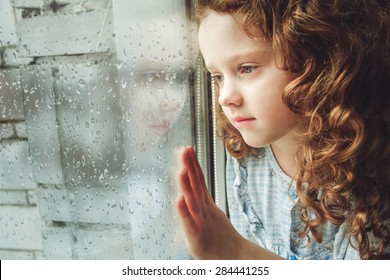 Sad Child Looking Out The Window. Toning Photo.