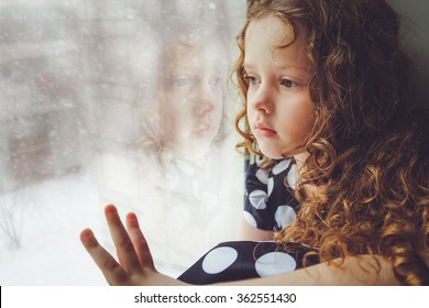 Sad Child Looking Out The Window On Falling Snow. Toning Photo Instagram Filter.