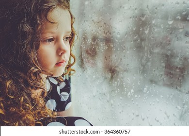 Sad child looking out the window on falling snow. Toning instagram filter.