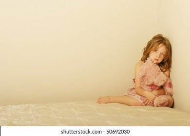 Sad Child Sitting Alone On Old Mattress With A Teddy Bear