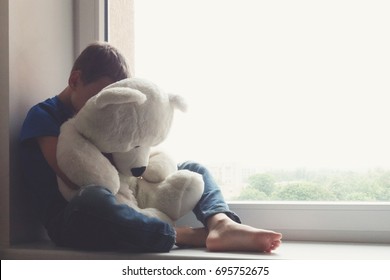 Sad Child Sitting On Window With Teddy Bear