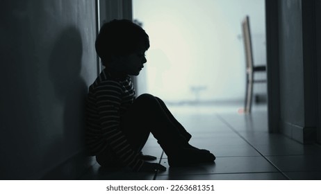 Sad child suffering from depression sitting alone in corridor feeling loneliness. Scared fearful small boy covering face in silhouette at home