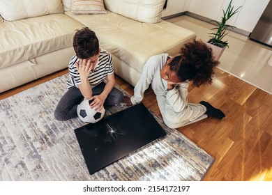 Sad Children Standing In Front Of A TV With Broken Screen Holding A Ball. Home Insurance Concept.