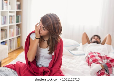 Sad couple after an argument in bed; woman sitting on the edge confused while man is lying in the background angry