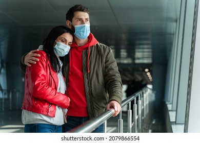 Sad Couple In Love Wearing Protective Mask Embracing At The Airport Hall While Standing In Front Of The Window And Waiting For Something