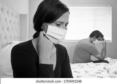 Sad Couple In Self Isolation Wearing Face Mask Bored In Home Bedroom Sitting On Bed.