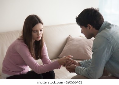 Sad couple sitting opposite one another, man holding hands of a woman. Loving husband comforting troubled young wife, compassionate boyfriend supporting crying girl, abortion or infertility problem