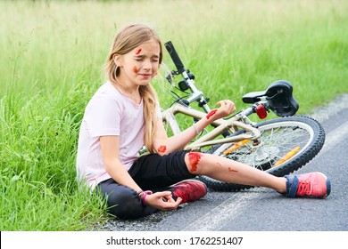 Sad crying little child girl fell from the bike in the summer park. Bleeding on hands and feet. Bicycle accident. Injuries while cycling. Accidents and injuries to children during summer activities