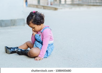 Sad Dark Skinned Toddler Baby Girl Sitting On The Ground. No To Violence Against Children Concept.