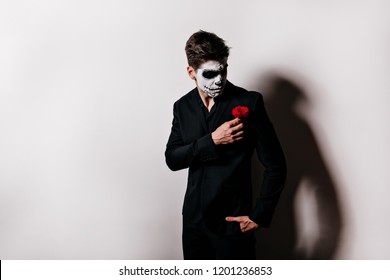 Sad Dark-haired Man Touching Flower On His Jacket. Caucasian Male Model With Zombie Makeup Posing After Halloween Event.