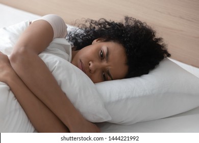 Sad depressed african american young woman hugging pillow lying in bed alone, upset frustrated black lady feeling lonely anxious suffer from insomnia trying to sleep thinking of problem in bedroom