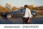 Sad depressed African-American businessman looking at camera being unhappy with broken car with opened hood on background. Beautiful aggressive African man in suit in trouble.