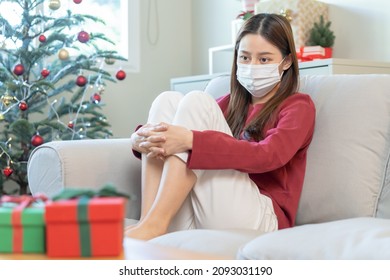 Sad, Depressed In Christmas 2021, Sickness Or Ill Asian Young Woman, Girl Celebrating Holiday Sitting On Sofa At Home Alone In Lockdown. COVID-19, Social Distancing Loneliness And Sadness.