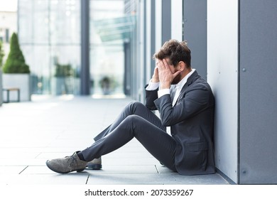 Sad Depressed Entrepreneur In Formal Suit Worker Man Sitting Near Outdoors Street Near Modern Office Business Center. Upset Male Businessman Lost Job Due Financial Crisis Employee Has Problem. Outside