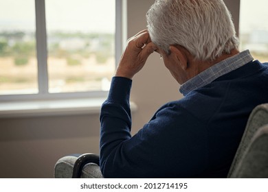 Sad and depressed old man sitting on armchair in living room feeling hurt and lonely. Frustrated senior sitting on sofa at nursing home with head leaning on his hand while looking through the window. - Powered by Shutterstock