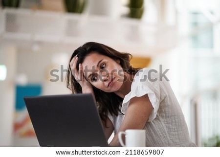 sad depressed remote working brown hair woman sitting disappointed with headache infront of a laptop or notebook on her work desk in modern airy bright living room home office