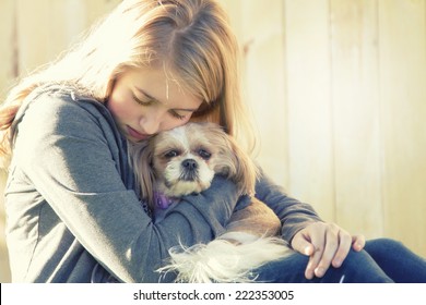 A sad or depressed teenage girl hugging a small dog in an outdoor setting