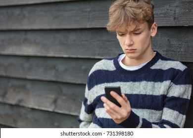 Sad Depressed Thoughtful Male Boy Teenager Blond Child Outside Using Mobile Cell Phone For Texting Or Social Media