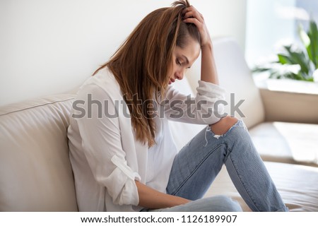 Sad depressed thoughtful young woman feeling bad at home, upset millennial lonely girl thinking of sorrow, regrets of mistake or worries about having psychological problem sitting alone on sofa